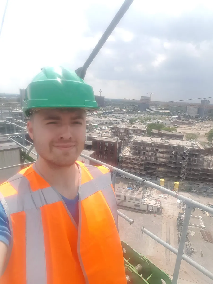 Jason Krijgsman on a construction site in Amsterdam in 2018, in a hard hat and high-visibility vest, photographed from the tower crane with the city behind him.